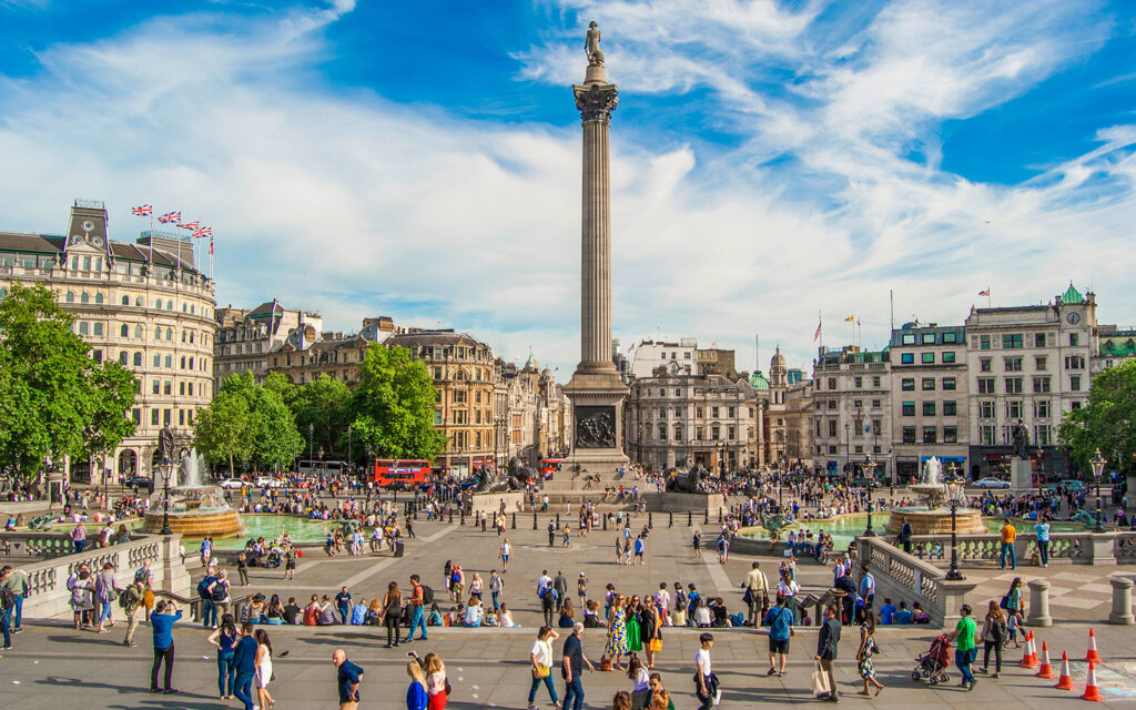 Trafalgar Square, London, with Nelson's Column and crowds enjoying the sunny day.